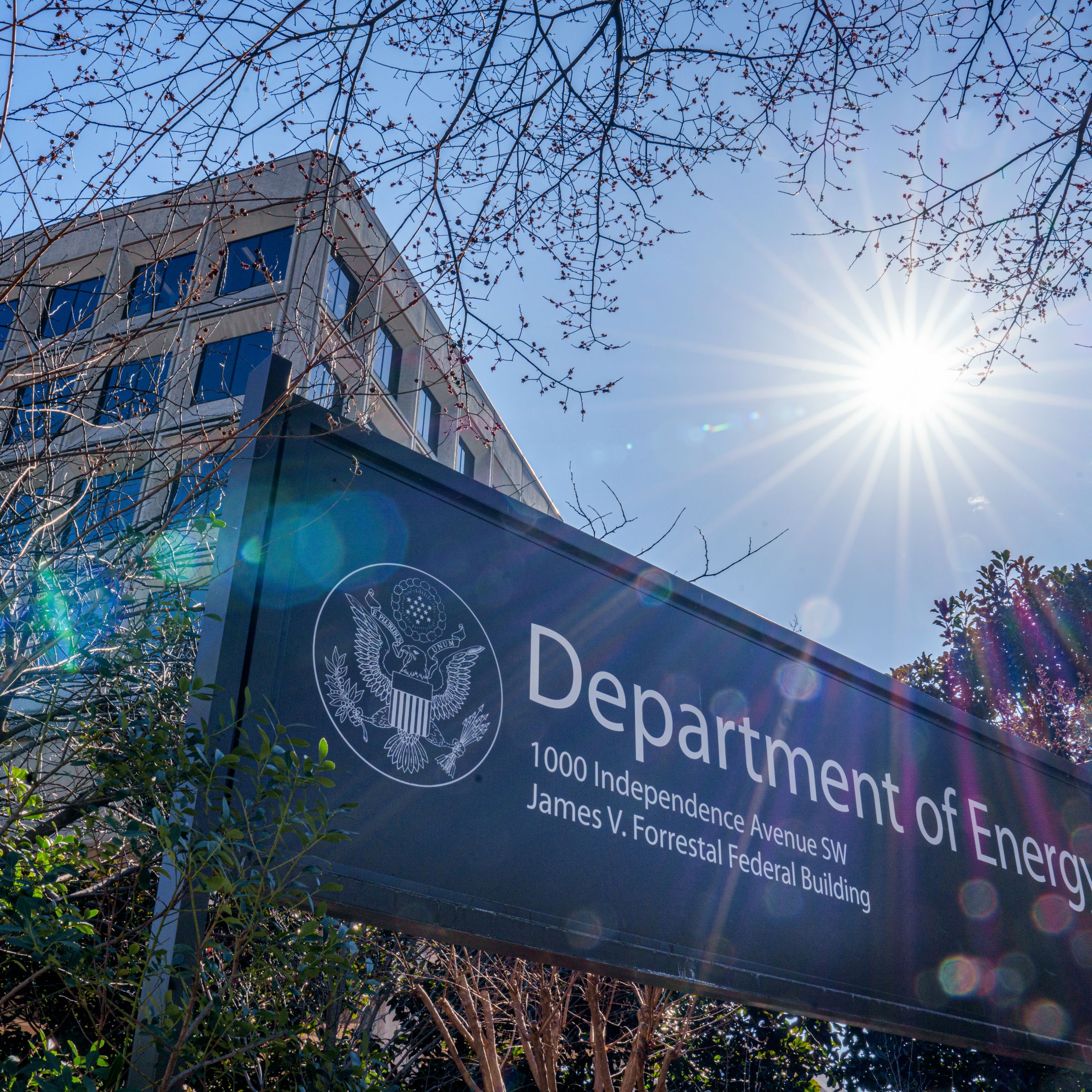 The sun flares over the sign marking the location of the US Department of Energy headquarters building