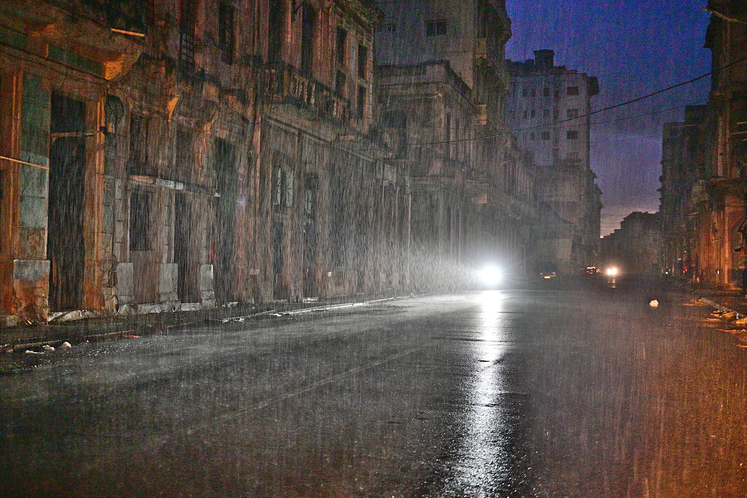 A motorcycle drives along a city street under pouring rain. 