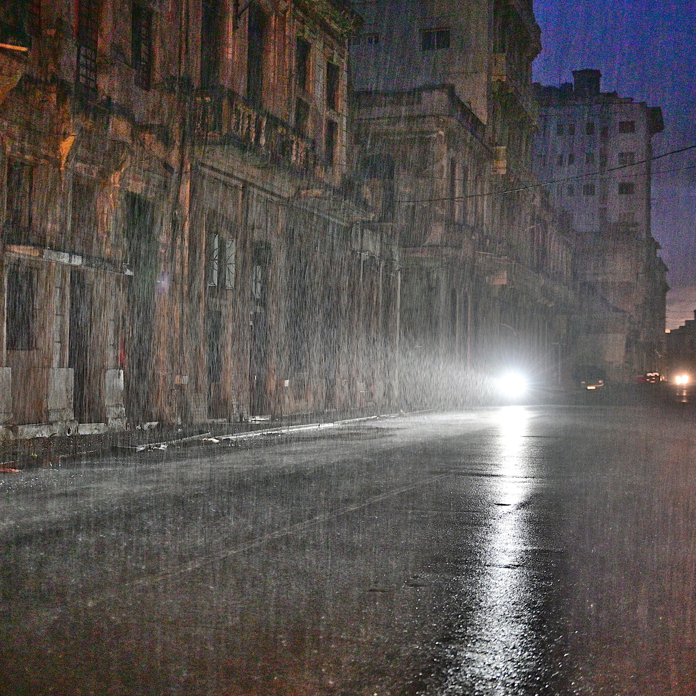 A motorcycle drives along a city street under pouring rain. 