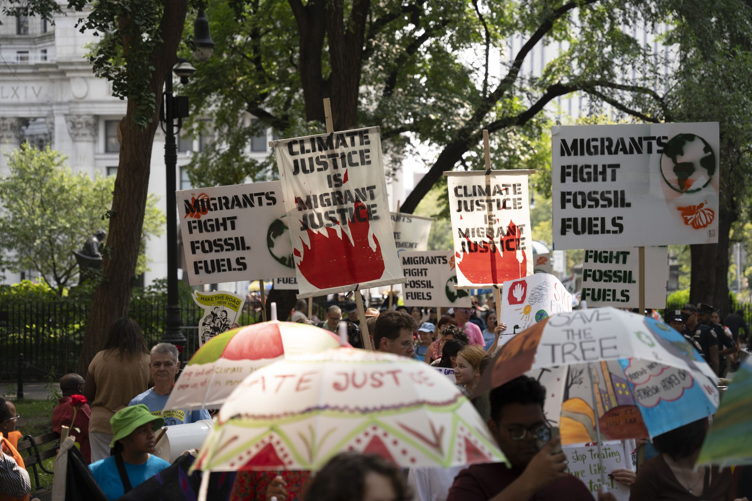 A crowd gathers with people carrying signs that say “climate justice is migrant justice” and “migrants fight fossil fuels.”