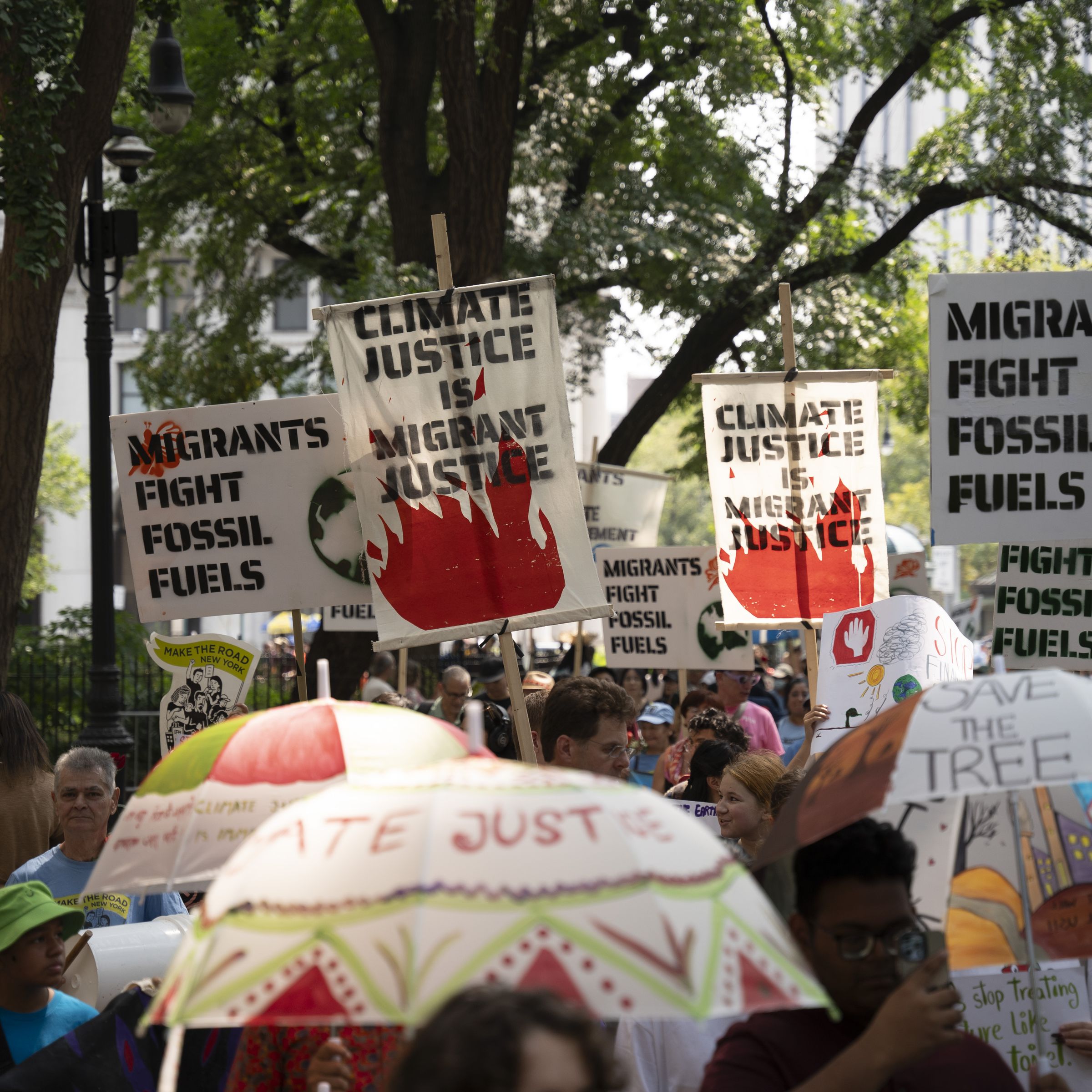 A crowd gathers with people carrying signs that say “climate justice is migrant justice” and “migrants fight fossil fuels.”