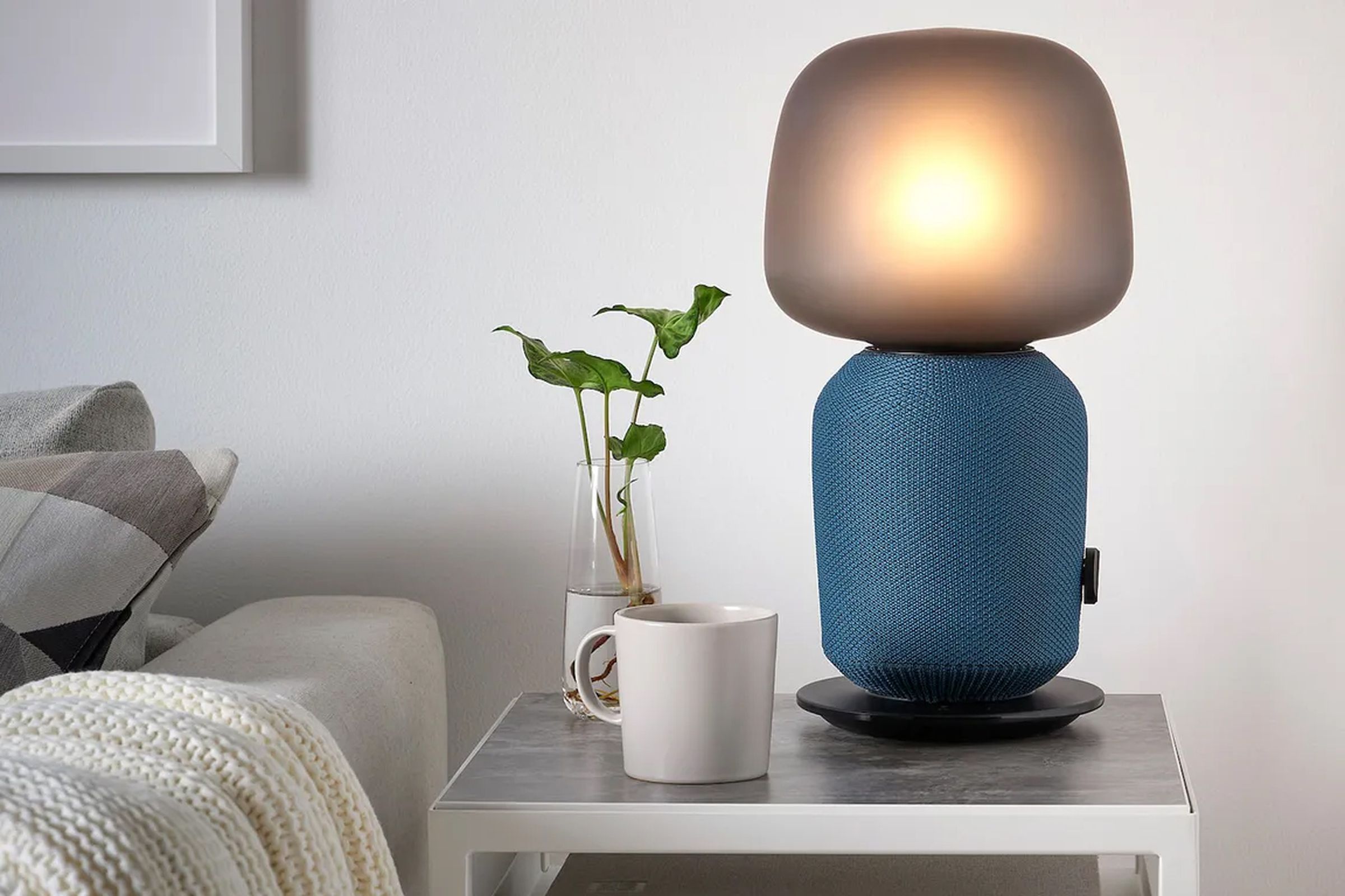 The Ikea Symfonisk speaker lamp in blue sitting on a bed’s side table.