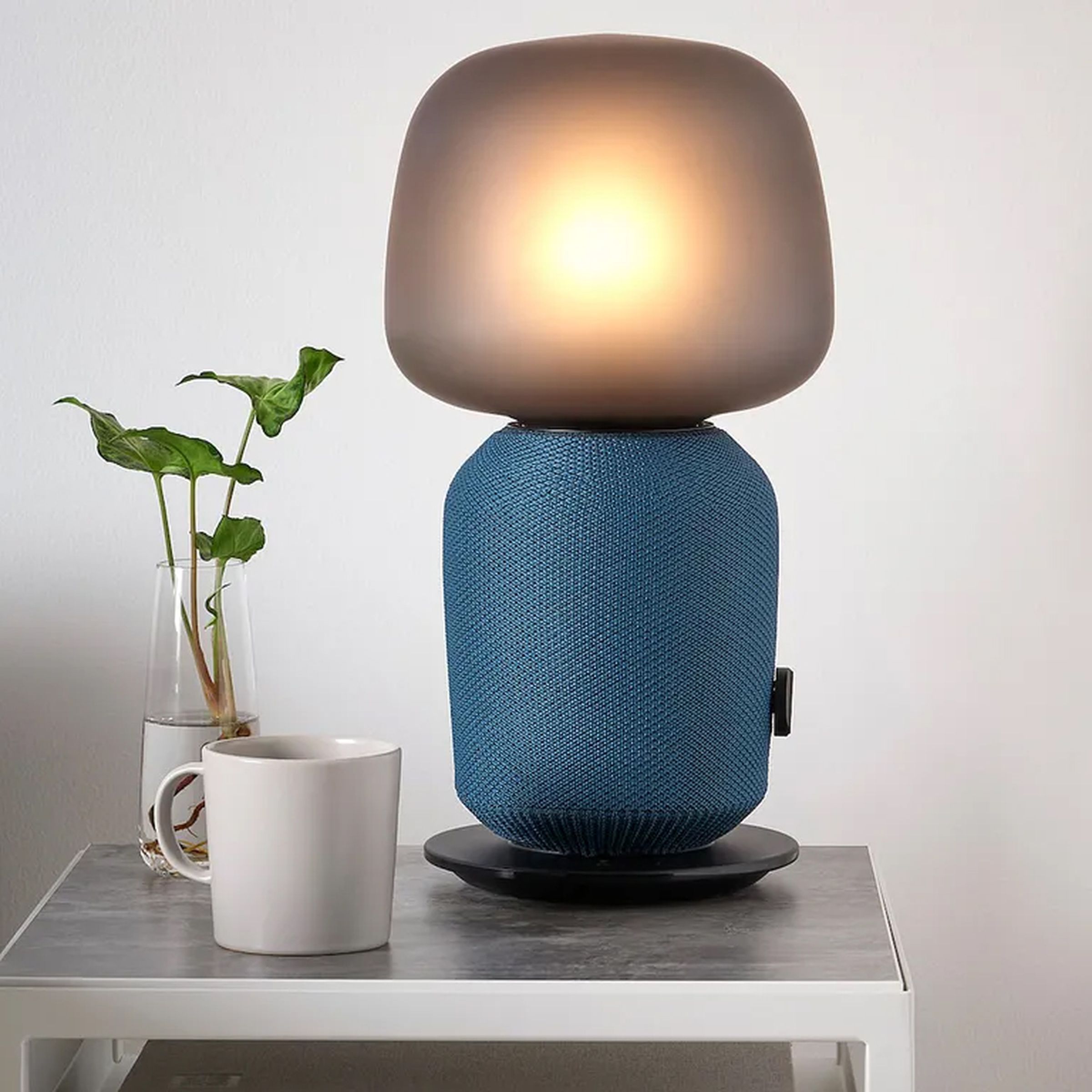 The Ikea Symfonisk speaker lamp in blue sitting on a bed’s side table.