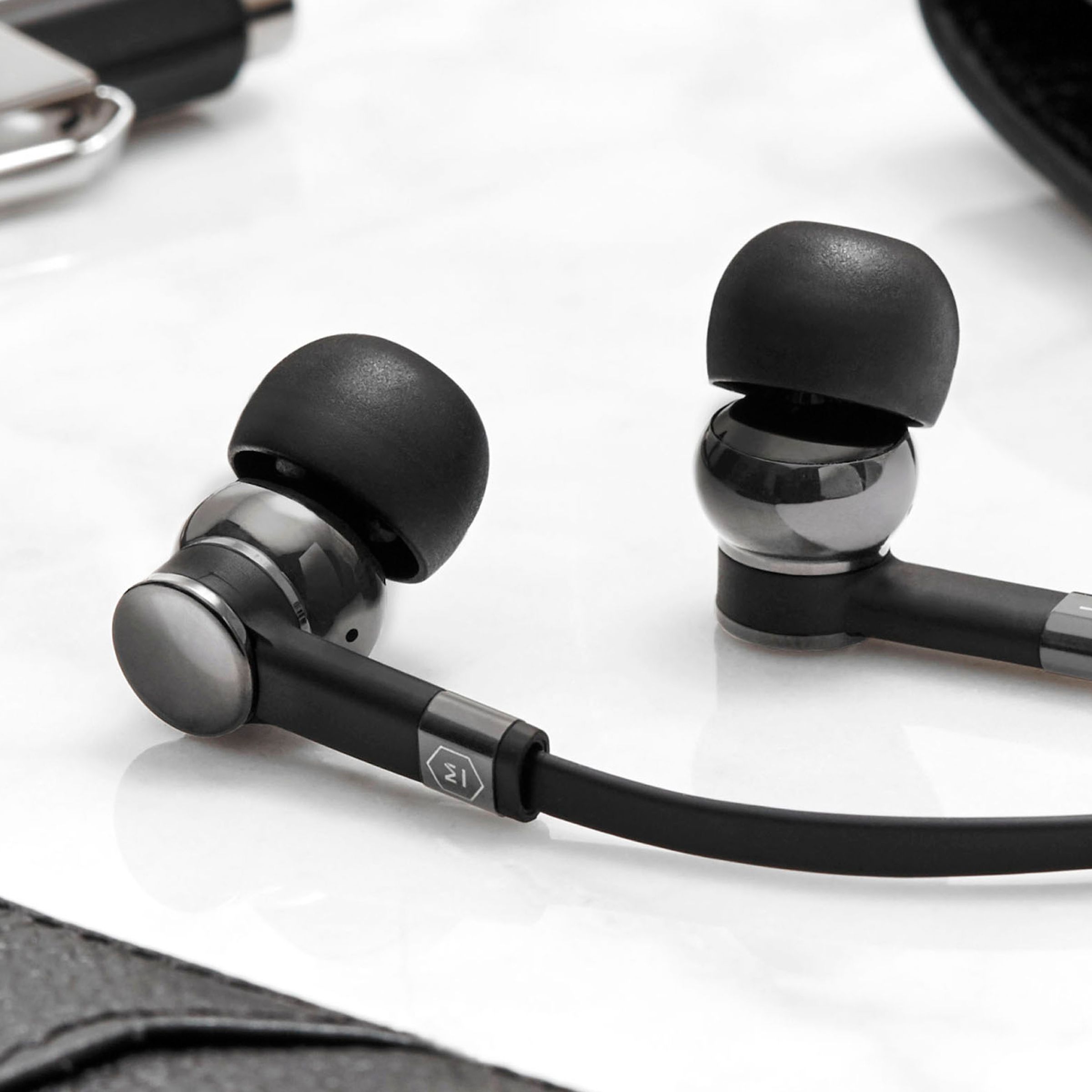 A close-up of Master &amp; Dynamic’s updated ME05 wired earphones on a white table.