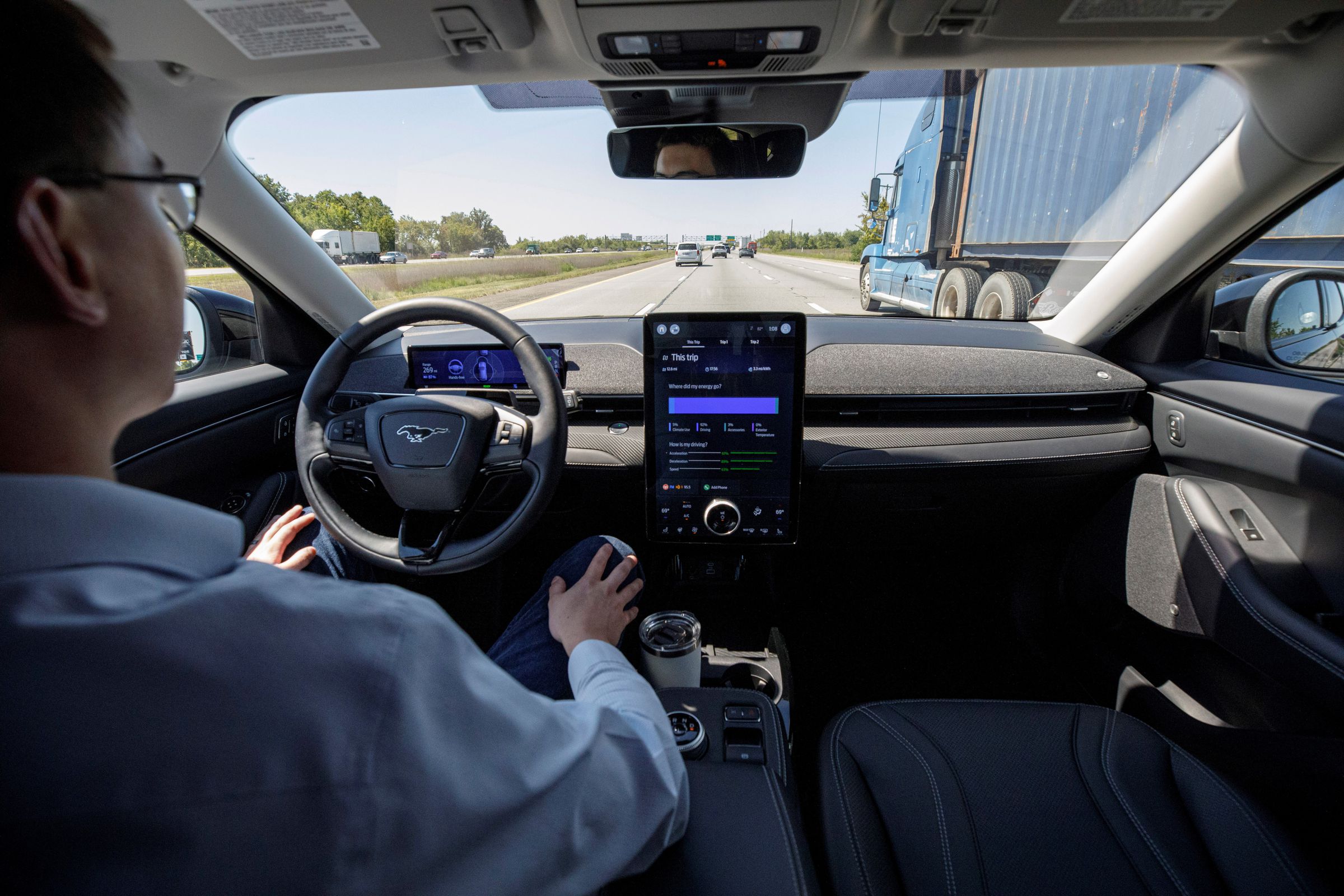 A back seat view of a man behind the wheel of a Ford Mustang on the highway