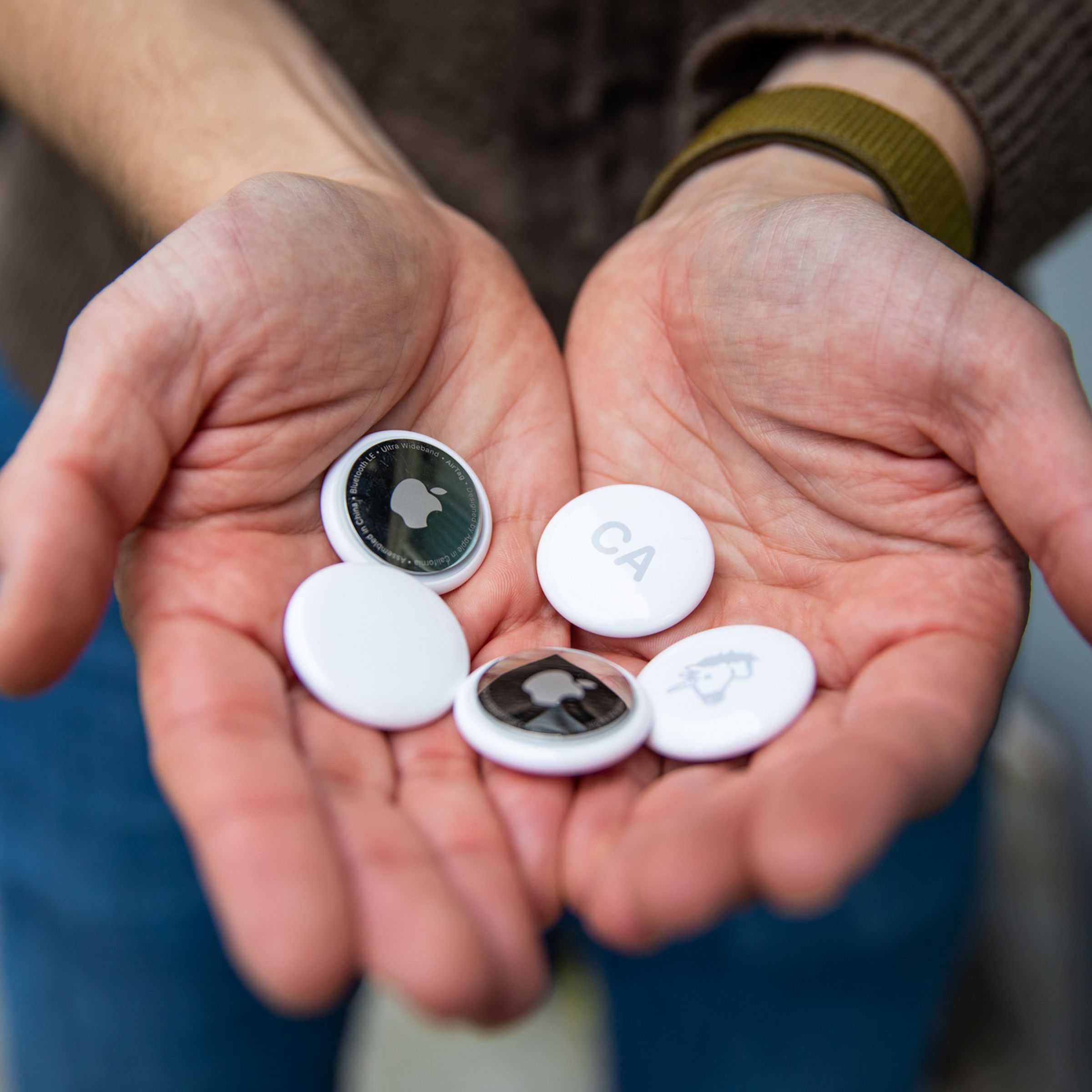 A close-up image depicting a set of hands holding a selection of Apple AirTags.